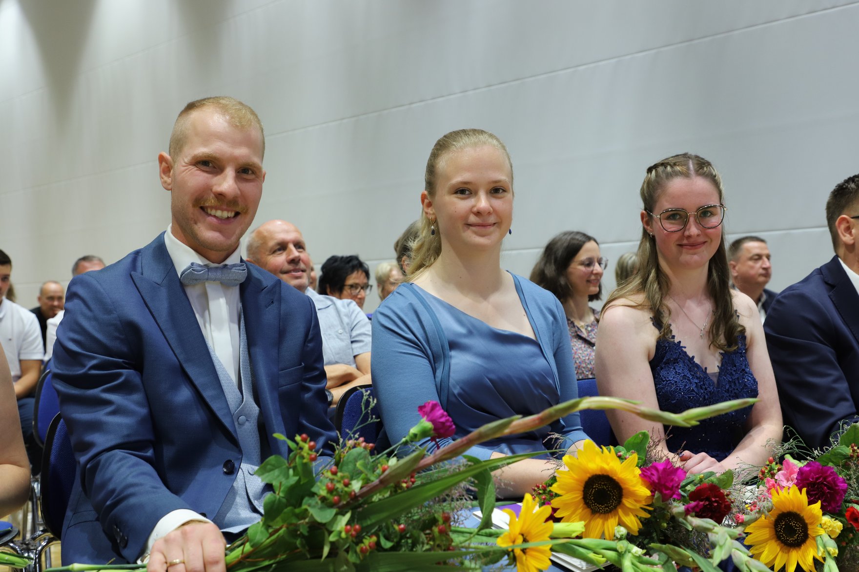Absolventinnen und Absolventen halten freudestrahlend ihr Abschlusszeugnis und Blumensträuße in ihren Händen.