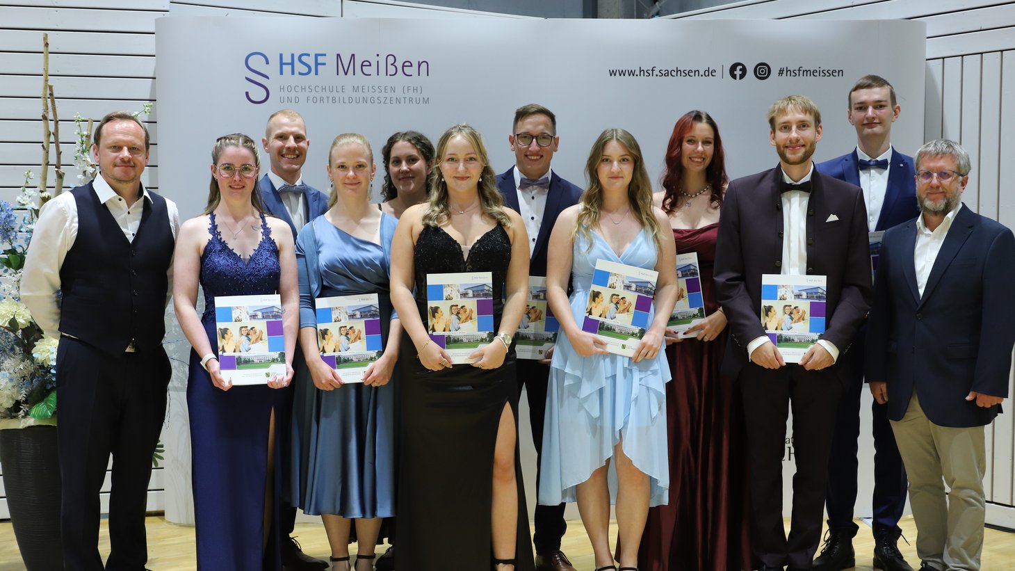 Gruppenfoto vor Fotowand der HSF Meißen mit Absolventinnen und Absolventen des Studiengangs "Sozialversicherung" und Vertretern der DRV