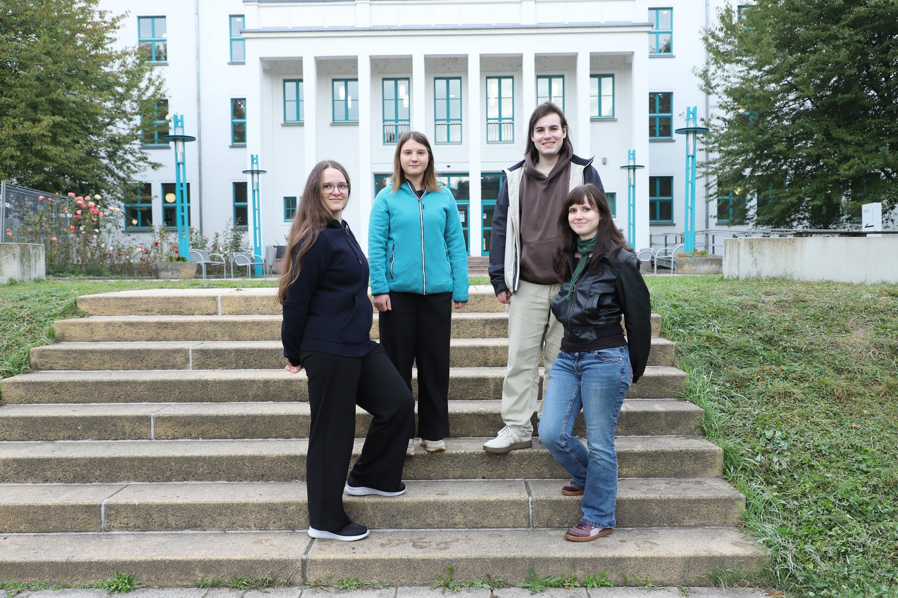 Azubis zum Gesundheitstag Die vier Azubis, die den Gesundheitstag mitgestaltet haben, stehen auf der Treppe vor dem großen weißen Hochschulgebäude der HSF Meißen.