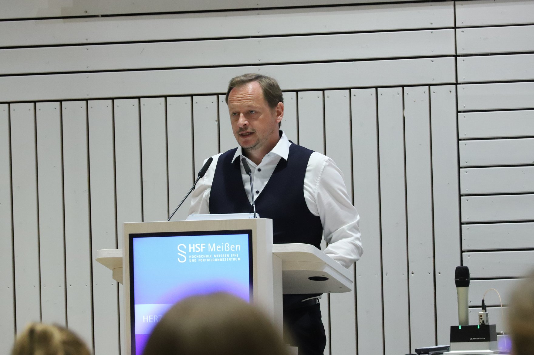 Fabian Wucholt, hält Grußwort an Absolventinnen und Absolventen des Studiengangs Sozialversicherung ab und steht vor den geladenen Gästen am Rednerpult.