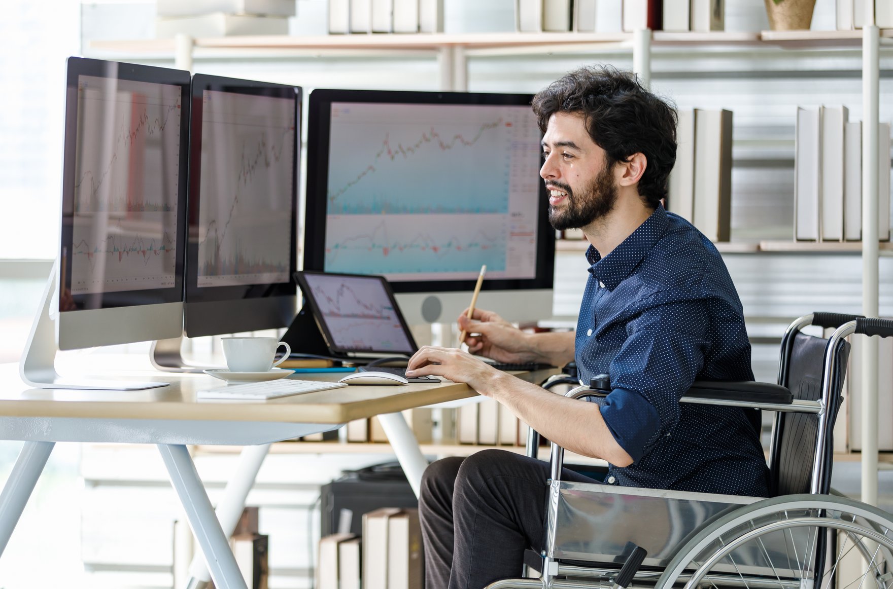 Studierender im Rollstuhl am Schreibtisch mit drei Monitoren Studierender im Rollstuhl