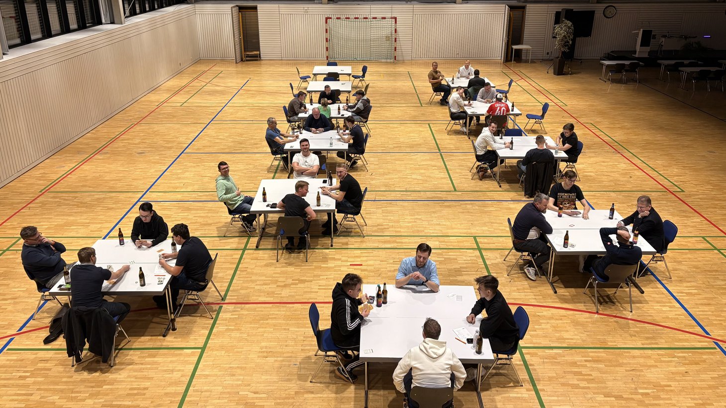 Teilnehmerinnen und Teilnehmer des Skatturniers sitzen verteilt an Tischen in der Mehrzweckhalle der HSF Meißen