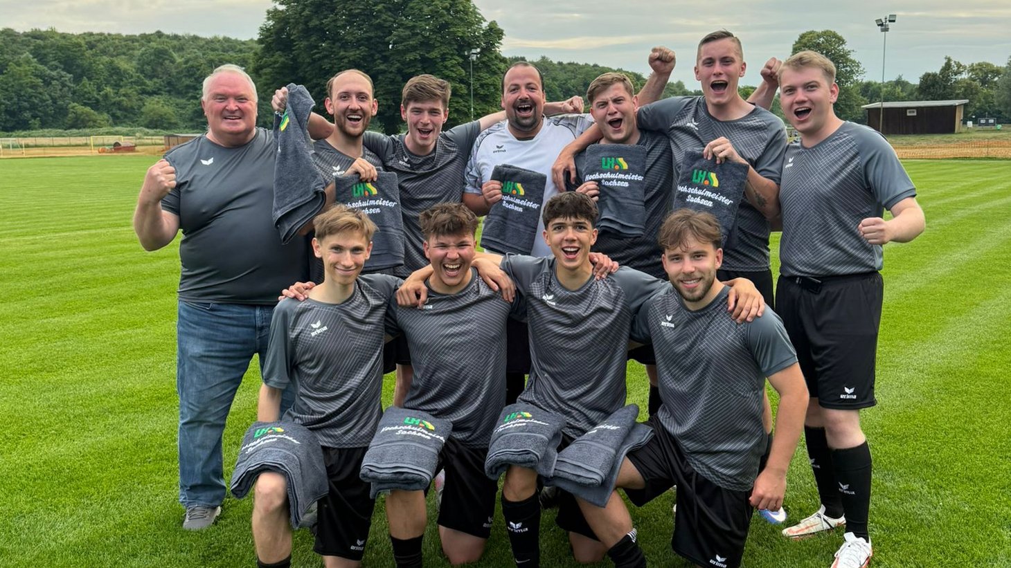 Ein Fußballteam steht auf einem Fußballplatz und posiert jubelnd in die Kamera. 