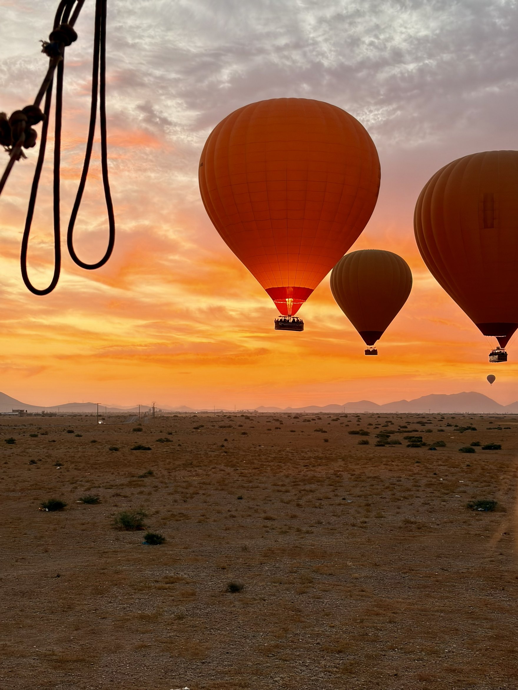 Mehrere Heißluftballons schweben bei Sonnenaufgang über einer weiten Landschaft. Der orangefarbene Himmel sorgt für eine stimmungsvolle Kulisse während der Ballonfahrt.