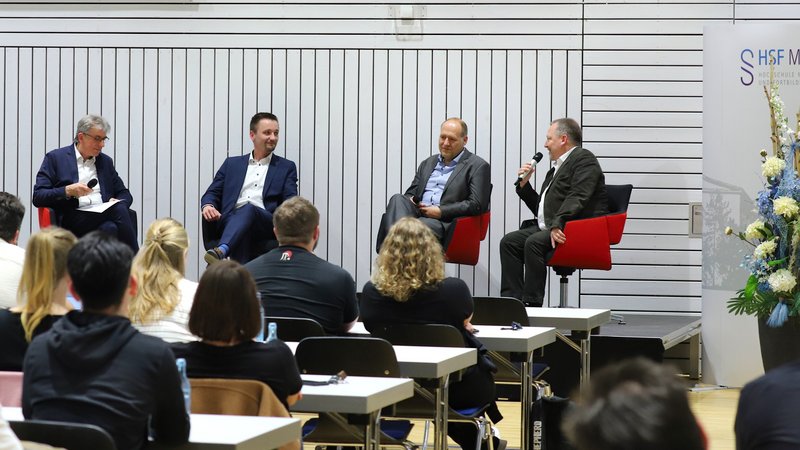 Podiumsdiskussion mit vier Podiumsteilnehmern auf der Bühne, im Vordergrund Zuschauende